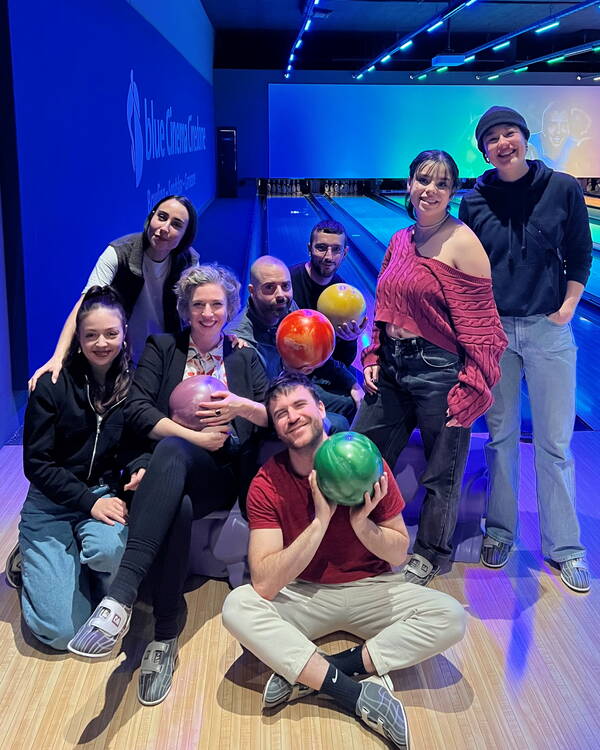 Das Team West posiert lachend vor einer Bowlingbahn. Vier Personen halten Bowlingkugeln in der Hand. 