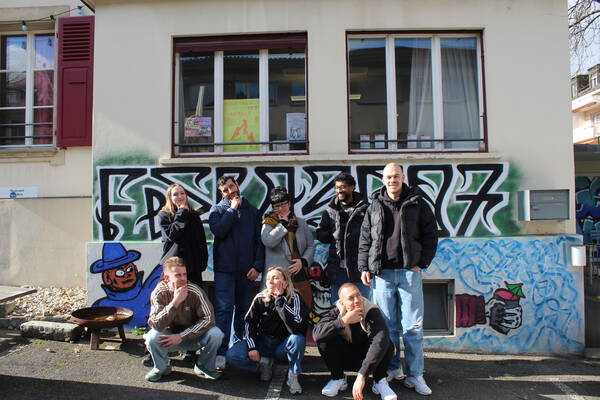 Die Mitarbeitenden des Teams Mitte stehen und sitzen lachend vor dem Jugendhaus Hopfenrain. 