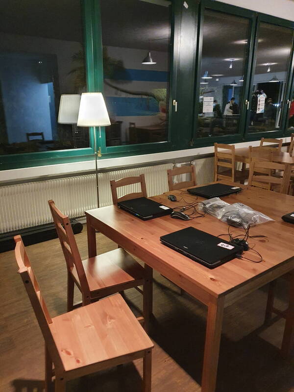 Die Räumlichkeit der Infothek mit einem Tisch und Stühlen. auf dem Tisch stehen drei Laptops 