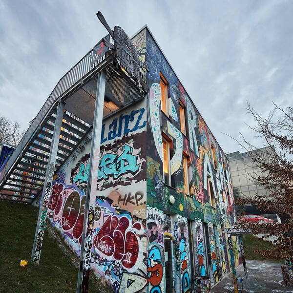 Das Jugendzentrum newgraffiti von aussen. Die Fassade ist mit Graffiti besprayt und eine Treppe führt aussen am Haus in das Obergeschoss. Das Jugendzentrum newgraffiti von aussen. Die Fassade ist mit Graffiti besprayt und eine Treppe führt aussen am Haus in das Obergeschoss.