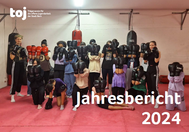 Das Titelbild des Jahresbericht 2024 vom toj. Eine Personengruppe steht in einem Boxkeller. Die Leute haben Boxhandschuhe an und halten diese auf Kopfhöhe.